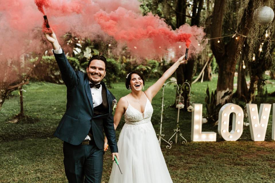 pareja de recién casado a la salida de la ceremonia con bombas de humo de colores