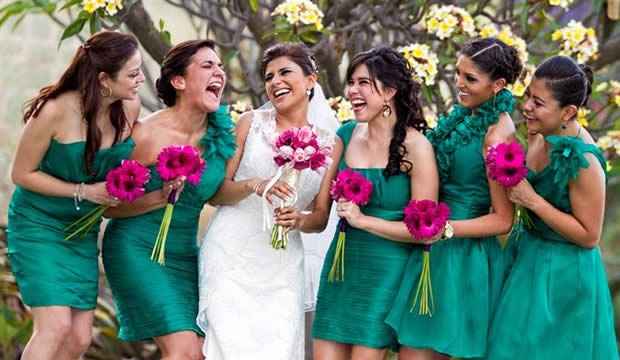 Las damas de honor con vestidos violetas se paran una al lado de la otra  debajo del arco de ramas verdes