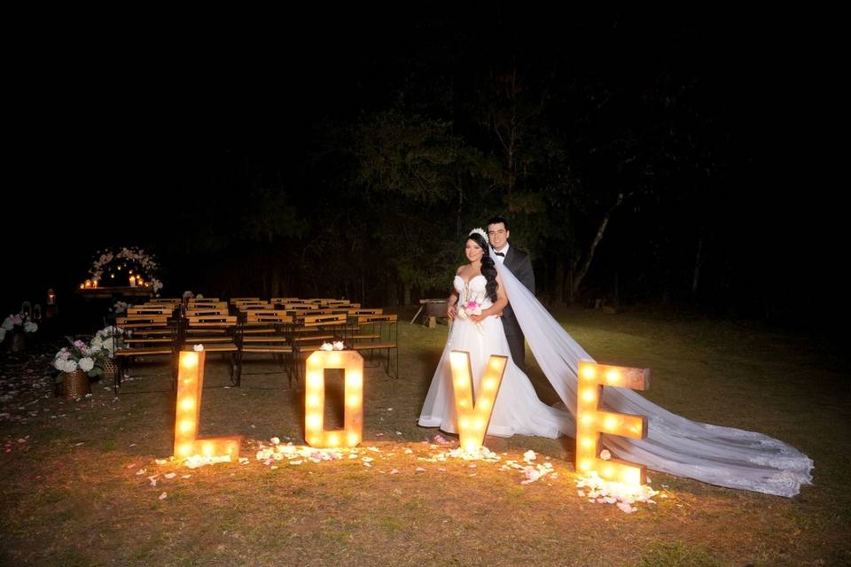 Novios posando con letras iluminadas de noche