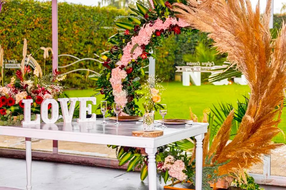 Arco de flores con mesa blanca y letrero blanco de love