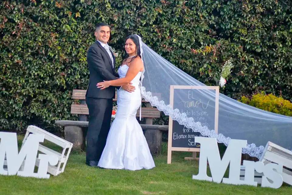 Novios posando en el jardín con letras grandes blancas