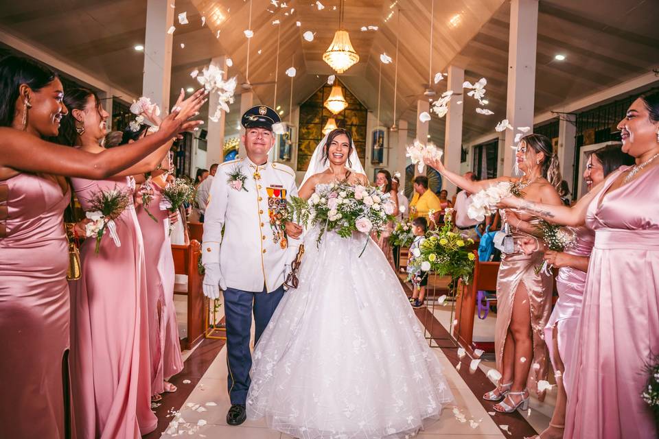 Novios festejando su boda mientras les avientan pétalos blancos