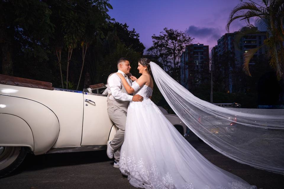 Pareja posando frente a un auto blanco