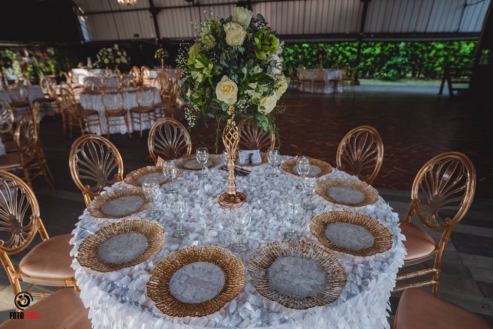 Mesas redondas con mantel blanco y platos dorados