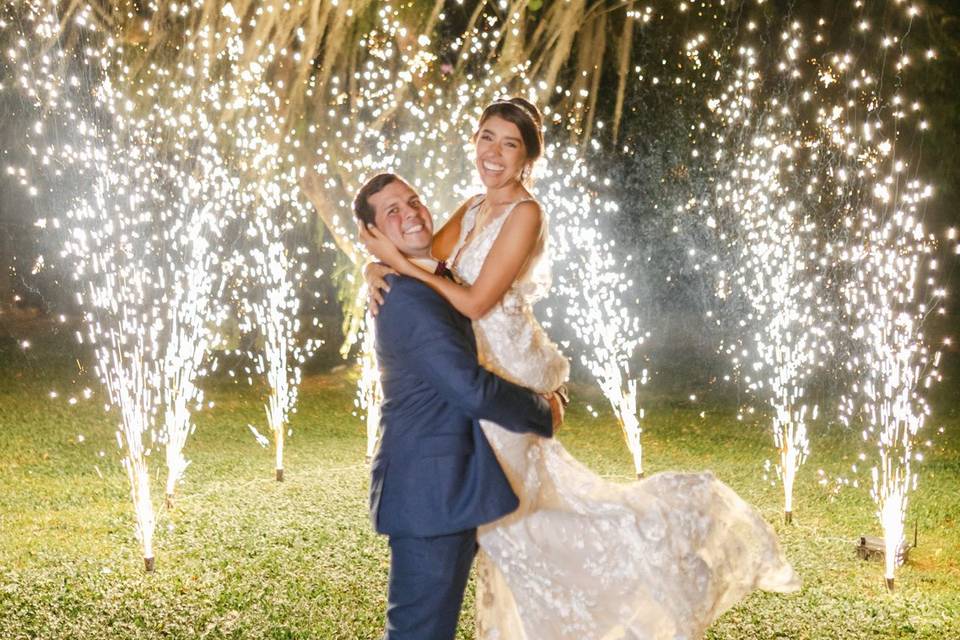 Novio cargando a la novia en el jardín con chisperos de fondo